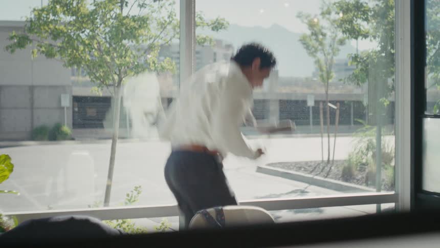 A man in a white shirt stands by a window in a welllit room celebrating after ending a phone call