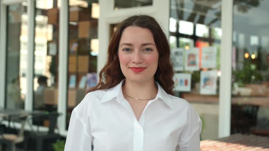 A woman in a white shirt stands before a glass door entrance to a store