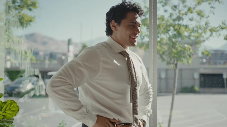 A man dressed in business attire stands alone in a modern office radiating happiness and excitement
