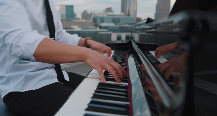 Hands of a person playing the piano on a terrace with buildings in the background