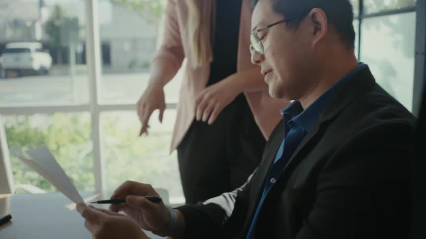 Woman discussing a document with a man sitting at an office desk