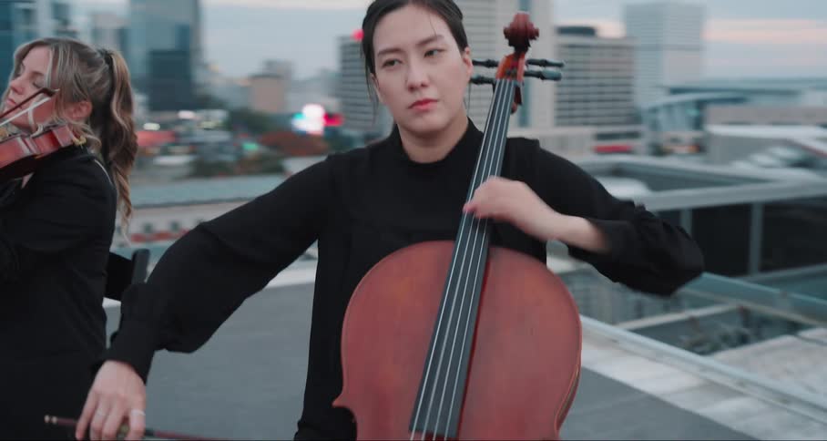 Musicians playing string instruments on a rooftop with an urban skyline behind them at sunset