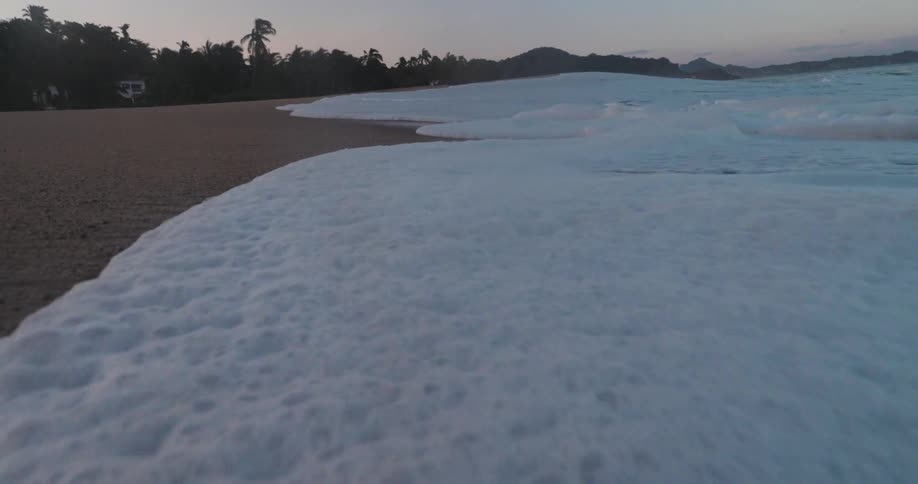 Sea waves with foam reaching the beach sand on a morning with the sky in shades of purple