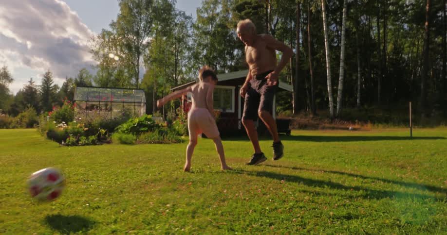 A child and an adult playing with a soccer ball on a grassy field during daytime under clear skies