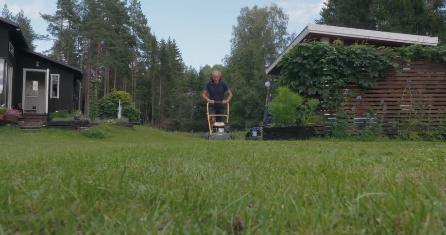 Elderly man in the backyard of a house cutting grass