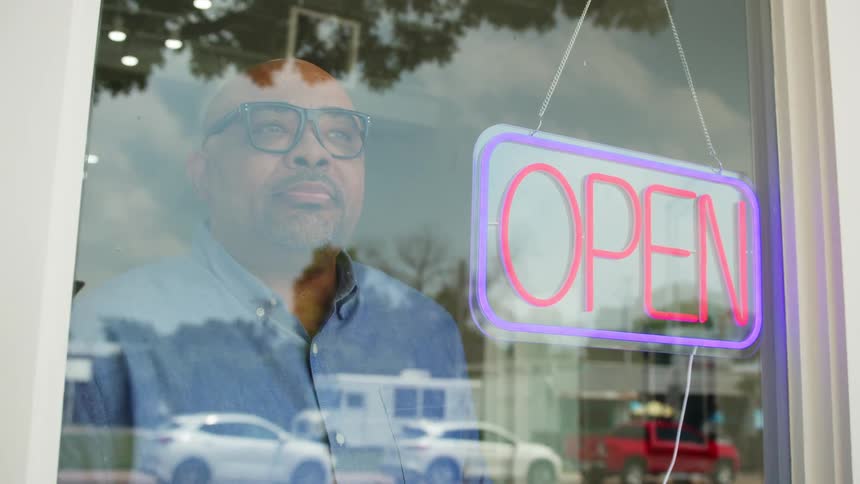 A person turns on a neon open sign hanging from the store door