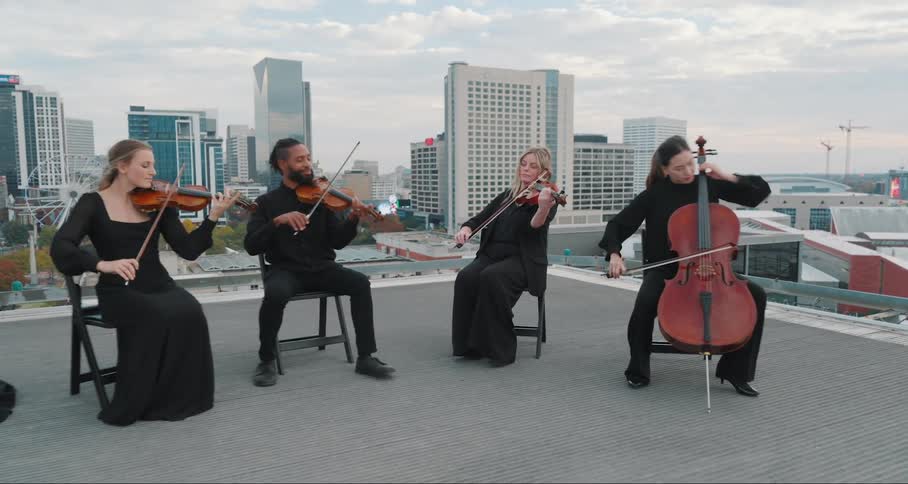 A string quartet performing on a rooftop with a city skyline in the background