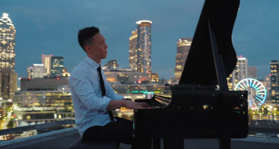 A man plays the piano and sings atop the roof of a building in the city