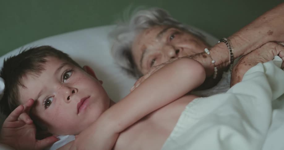 Grandmother lying in bed with her little grandson and stroking his arm