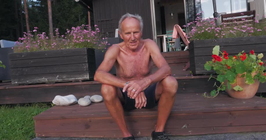 Portrait of an elderly man sitting on a wooden deck in an environment with trees around