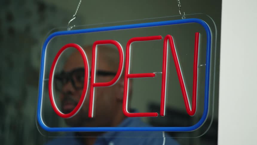 Man turning off the sign that says open on a store window