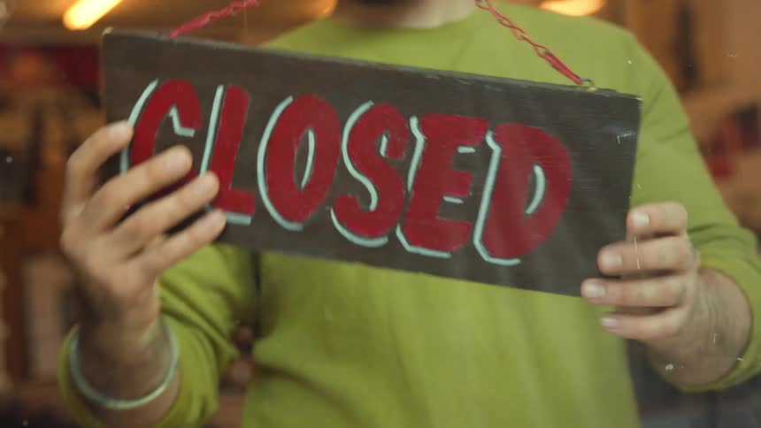 A business owner turns the sign from open to closed to close shop for the day.