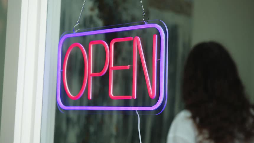 A young woman turns on an open sign hanging in a window