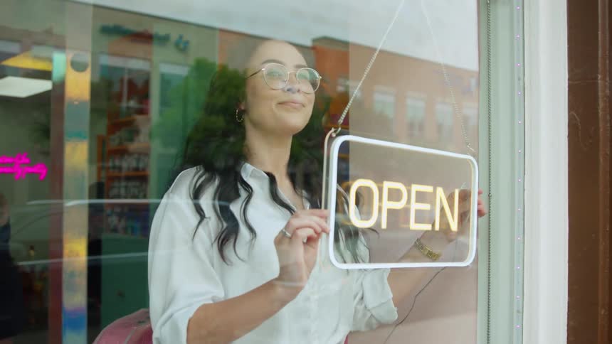 Smiling worker looks out store window while turning on the open sign