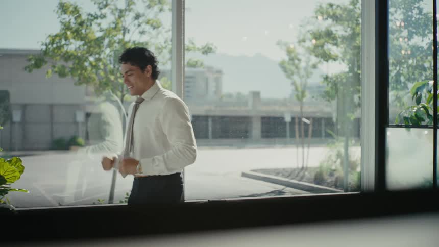 A man dressed in business attire stands alone in a modern office radiating happiness and excitement