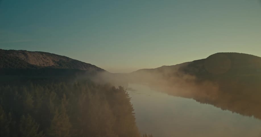 Low lying clouds float over a river passing the woods before it passes a rural town and farms