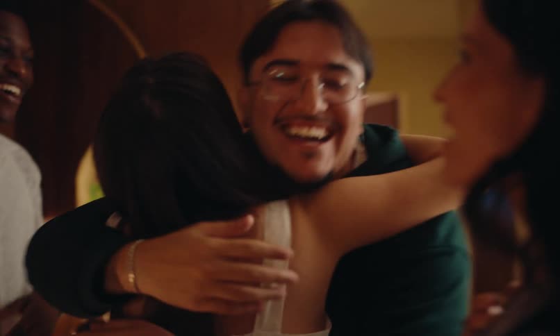 A couple arrives in a room and happily hugs their friends