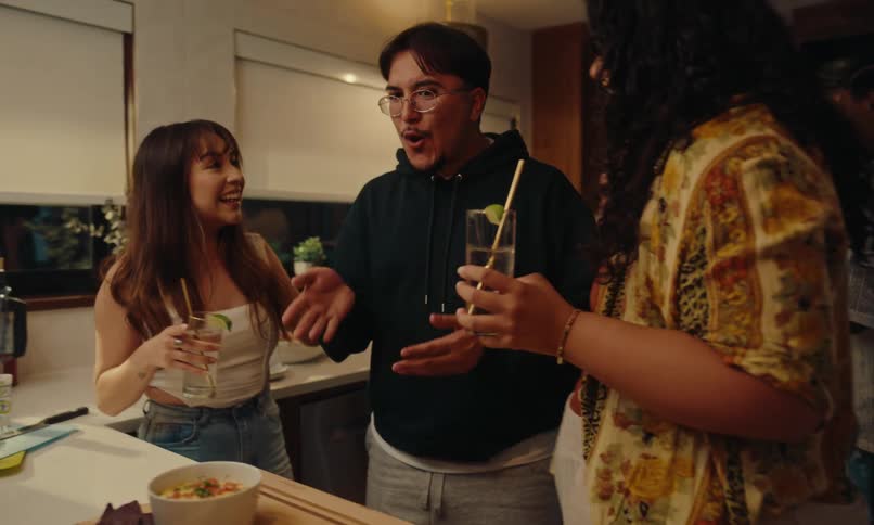 Friends in a kitchen at a house party holding drinks and with food options on the counter