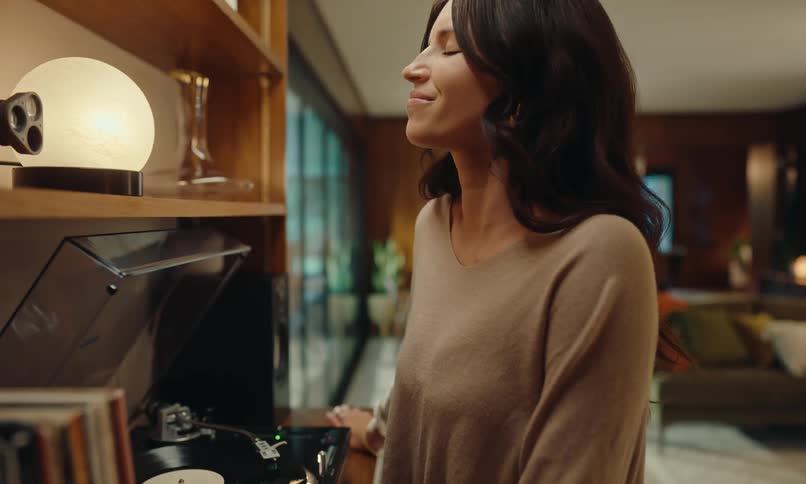 A woman is happily listening to a vinyl record and then she turns around and goes to the living room