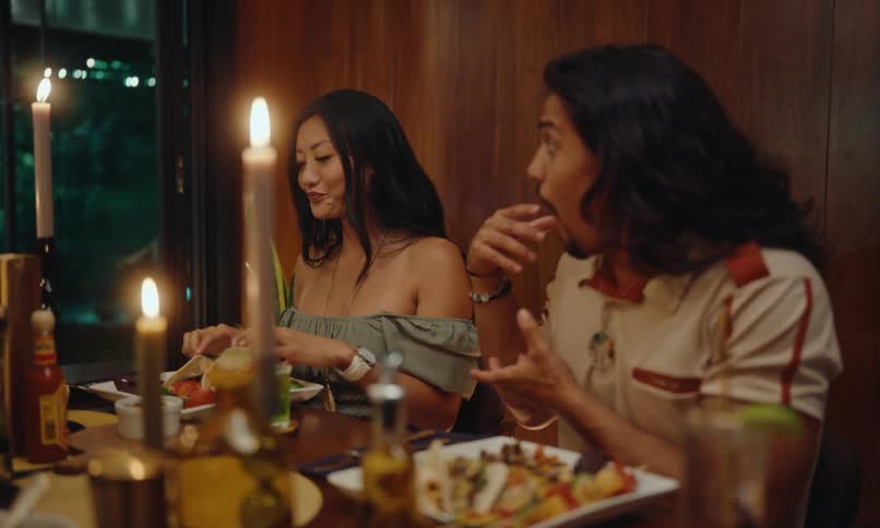 A couple seated at a dining table illuminated by canles having dinner with friends at a restaurant