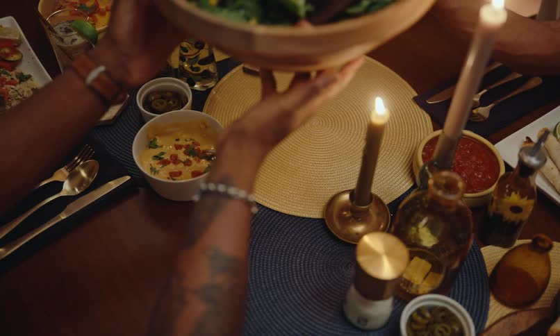 Dining table with candles and a persons hand picking up bowls of food