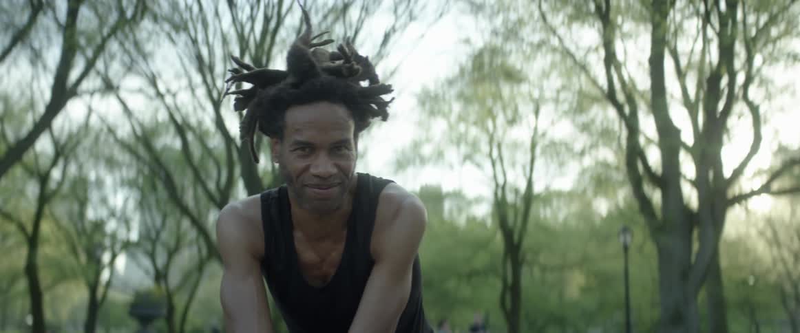 A man smiles outside under trees