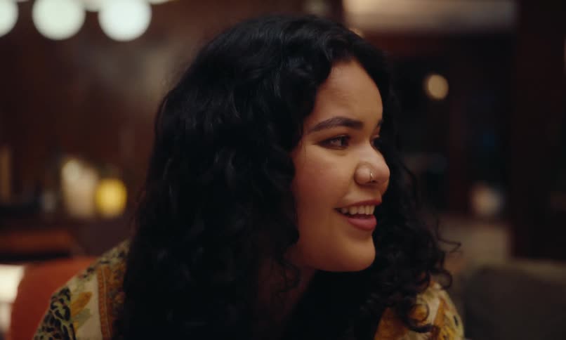 The face of a woman looking to her side where there are some people gathered sitting on a sofa