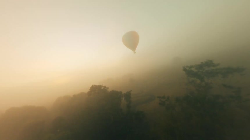 Aerial footage of a foggy landscape with a hot air balloon floating above it