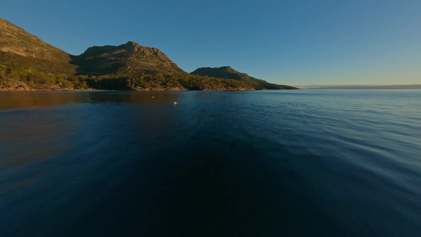 Flying low over the ocean, mountains covered in forests sit on a rocky coast