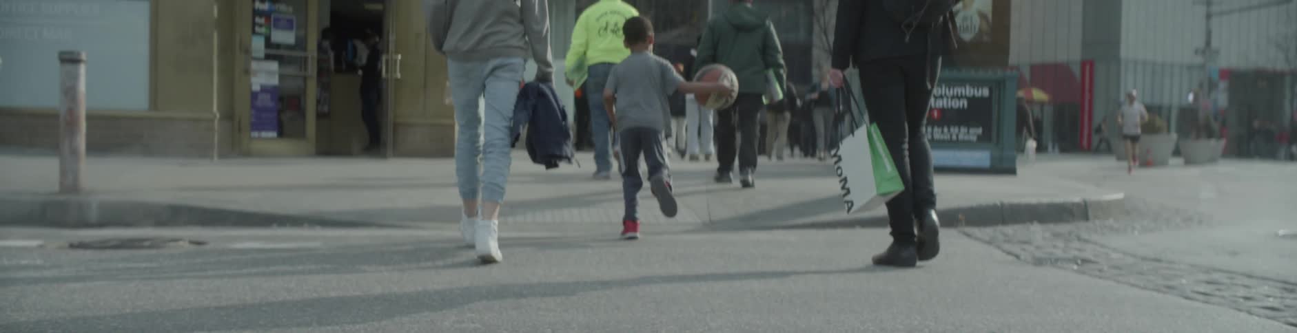 A group of people and a small child with a basketball are walking down the city street