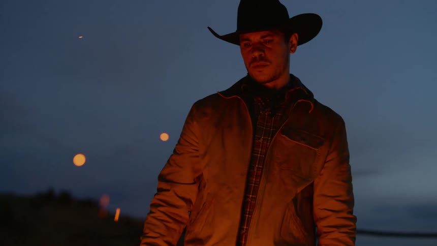 Rancher adds wood to the campfire while standing outdoors near a corral