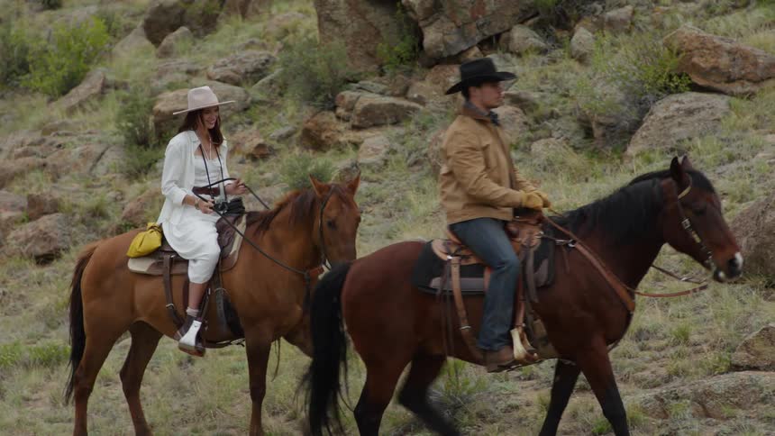 Man and woman each riding a horse up a hill