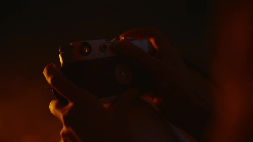 Pair of womans hands holding a vintage camera in front of a campfire at night