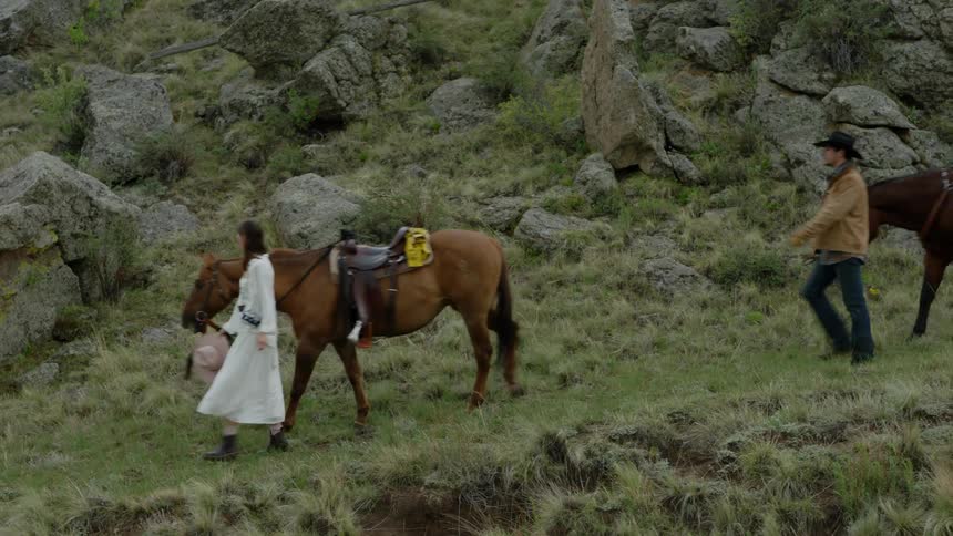 Man and woman walking on a hill and each of them carrying a horse by a rope