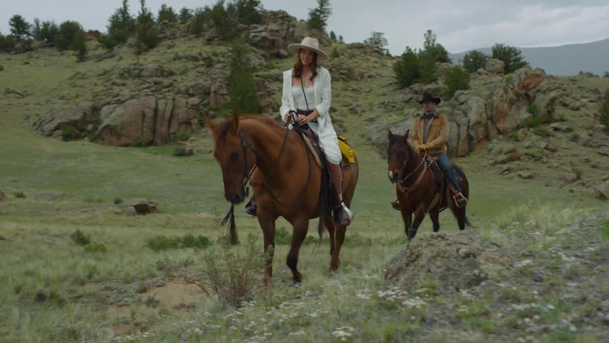 A man and a woman ride horses through a mountain valley