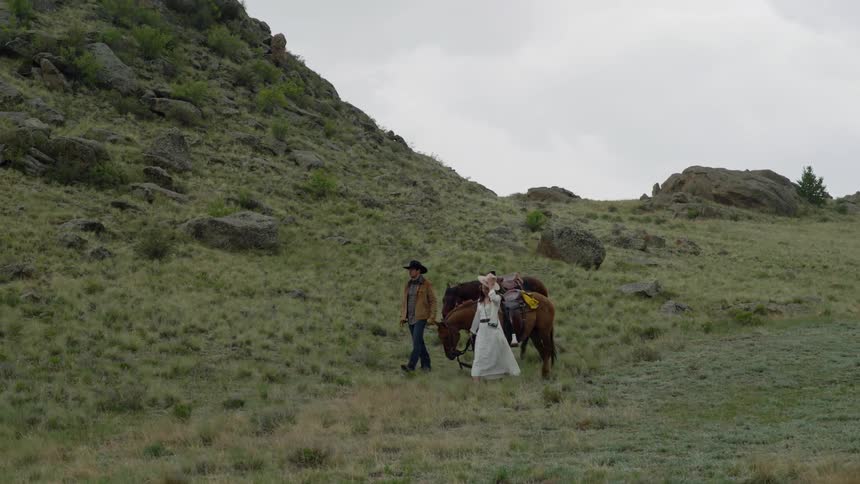 Man and woman walking in a field and each of them guiding a horse with their hands