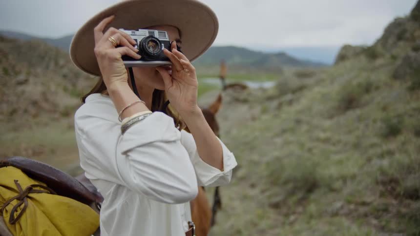 Woman next to a horse using a vintage camera in a mountainous environment
