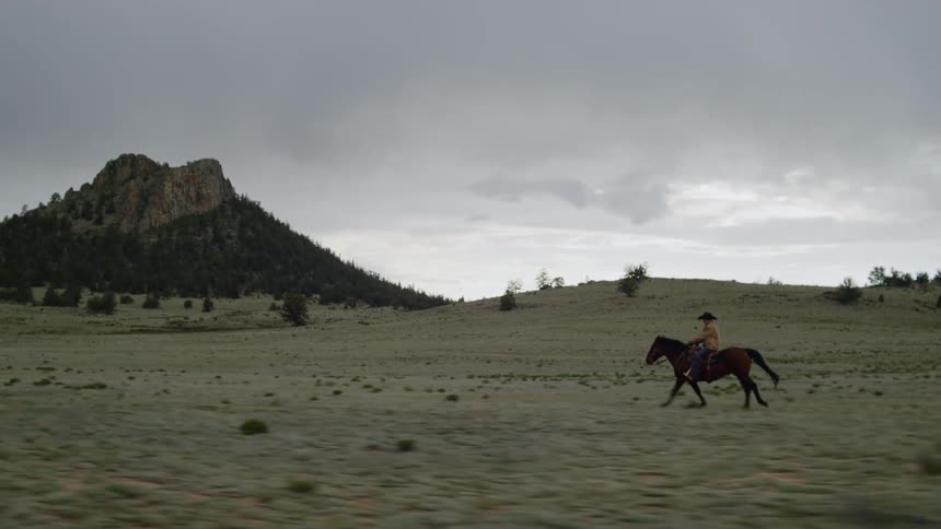 A man rides a horse across a large plain near hills and a mountain
