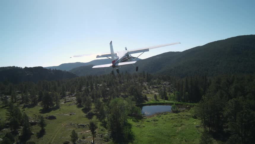 A small white singleengine plane flying over an area with a forest and a small lake