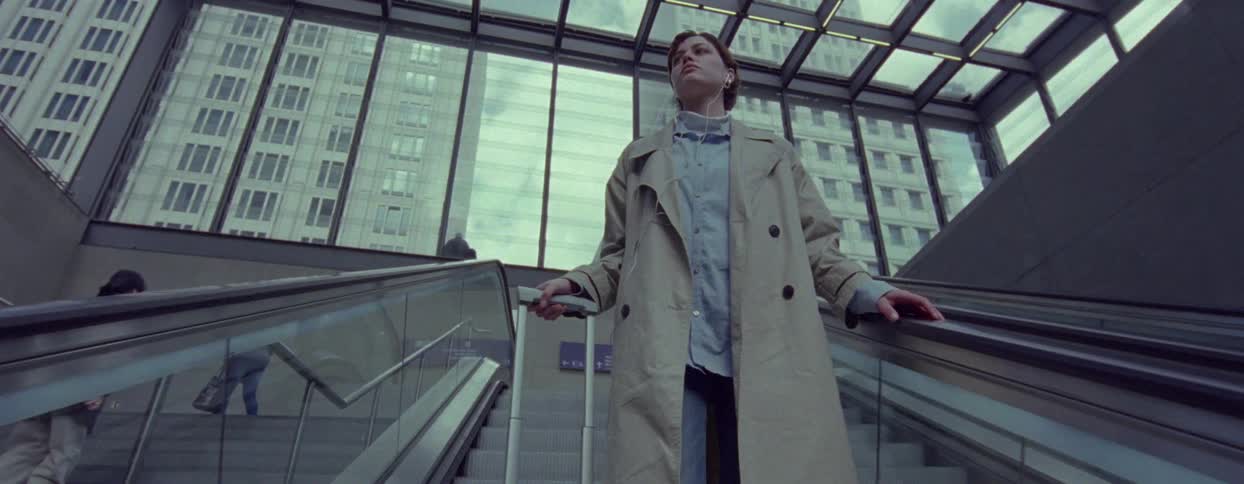 A woman standing on an escalator with a suitcase in a modern glassroofed building