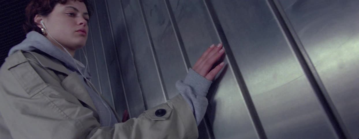 A young woman running her hand over the metal surface of a smooth textured wall