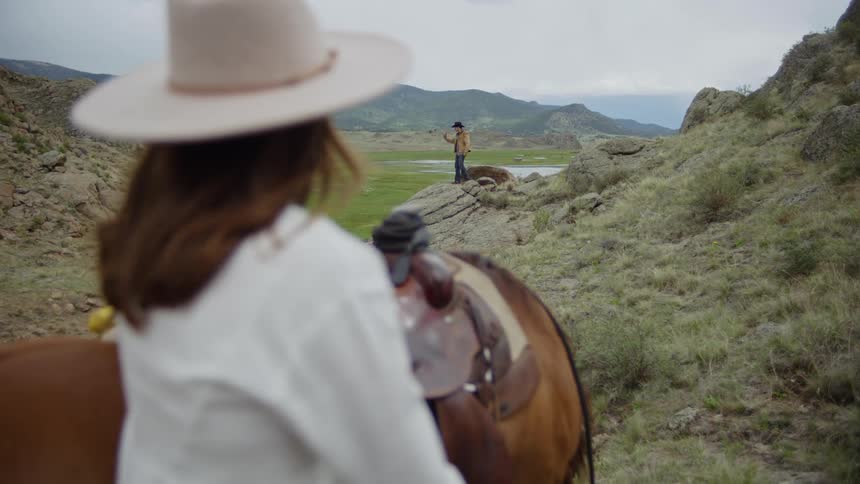 Woman next to a horse and in the background a man walking on a rock in a natural environment with mountains on the horizon