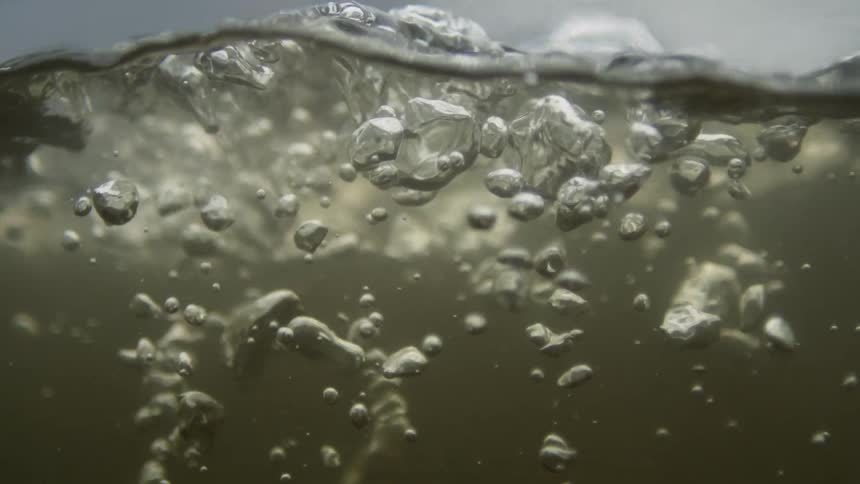Gray cloudy water is shown from halfway underwater with lots of bubbles