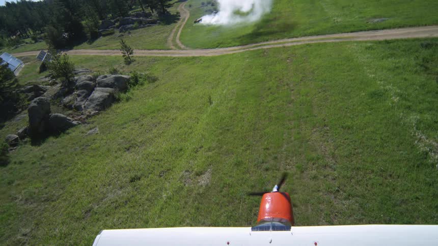 Aerial view of a small plane in motion for landing in a green field with trees around