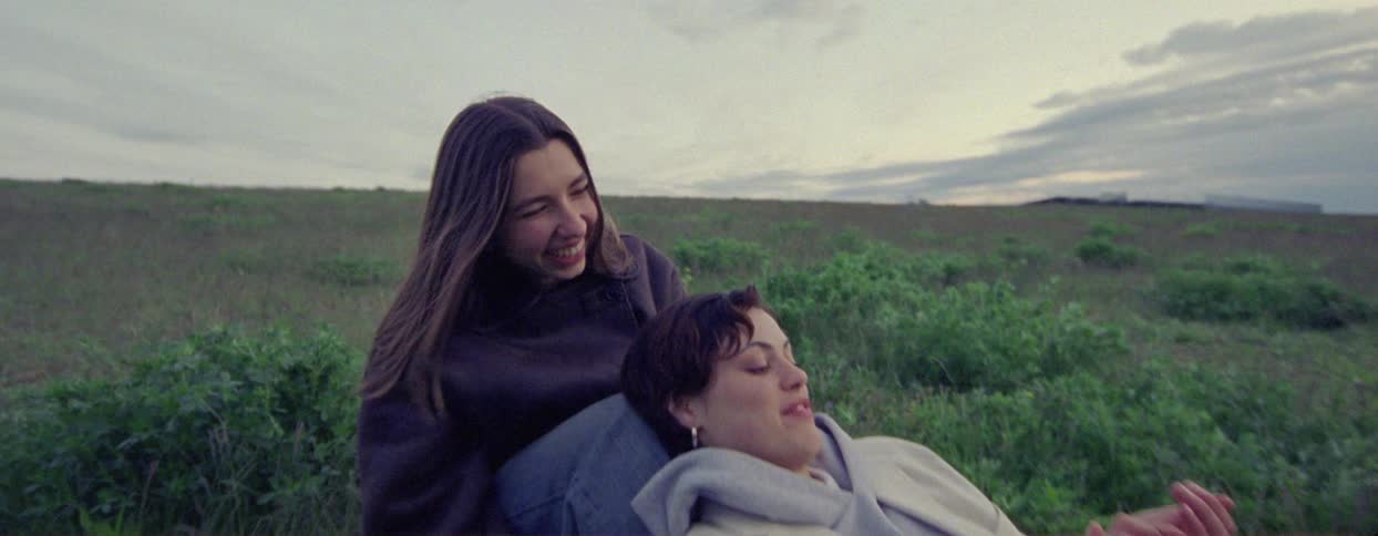 Two young girls sitting together in a field happily
