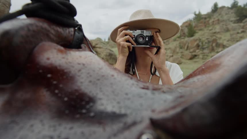 Woman in a hat using a vintage camera against a backdrop of hills