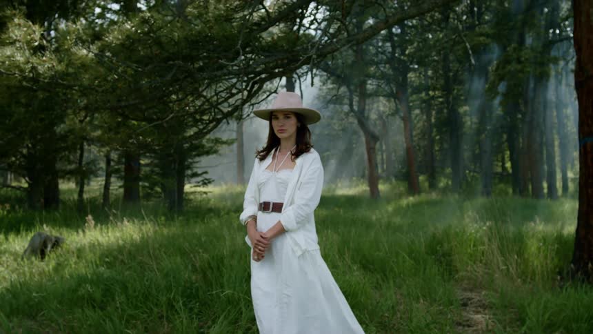 A white woman in a dress turns and stares in a forest