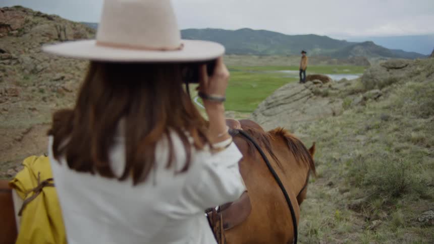 A woman snaps a photo of a man standing on a rock outcropping