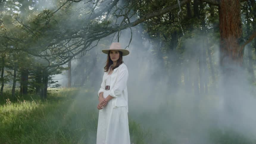 Woman in a hat and a long white dress in a forest with steam rising