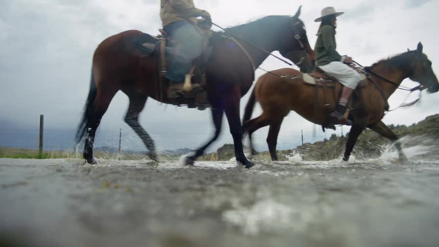 Two people riding horses across a river